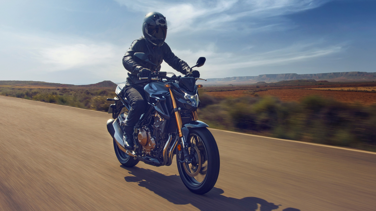 A rider head on riding a Honda motorcycle on a country road