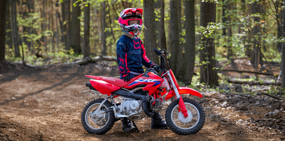 A young rider standing beside a CRF50F