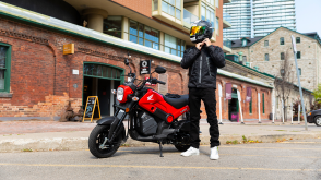 A rider taking off his helmet with a brick building as the background 