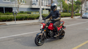 A rider riding a Honda Navi down a city street, side facing